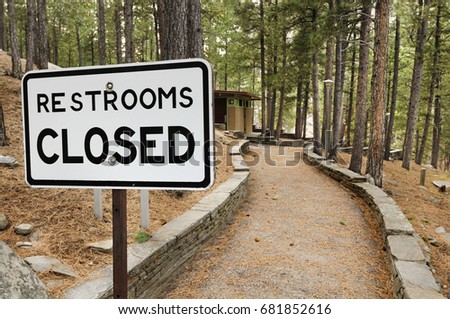 Sign indicating rest room closed in an empty park, with the building visible at the end of a long path