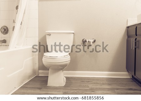 White flush toilet bowl with shower curtain, tub and empty roll on toilet paper holder. Modern bathroom interior in America. Empty toilet roll, concept for unexpected, emergency, humor. Vintage tone.