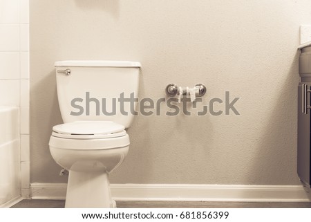 Close-up of white flush toilet bowl  and empty roll on toilet paper holder. Empty toilet paper roll in restroom. Modern bathroom interior in America. Out of toilet paper dilemma concept. Vintage tone.