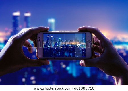 Photo camera of a smartphone. View through the screen at the time a young woman takes a photo of a city at night. Cityscape.