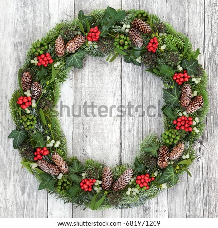 Christmas wreath decoration with holly, mistletoe, snow covered fir, blue spruce, ivy and pine cones on rustic white wood background.
