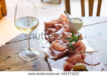 Flutes filled with sparkling prosecco, in a restaurant in Conegliano, and starter dish on a cutting board with salami, Trieste's ham, raw ham of Parma and mortadella, with horseradish as a sauce Royalty-Free Stock Photo #681973222