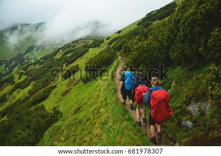 Tree friends walking together in mountains with big rucksack with rain cover - green meadow all around - tourist photo with copy space.