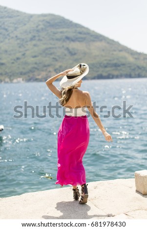 Young attractive woman with a hat poses by the sea at sunny day
