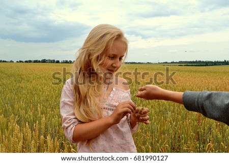 Beautiful girl with long blond hair in summer in a wheat field with a boy playing.