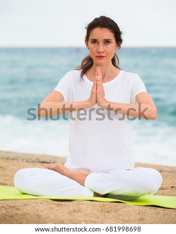 Female in white T-shirt is sitting and practicing meditation on the beach.