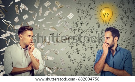 Side profile of two serious businessmen looking at each other one under money rain another with bright ideas