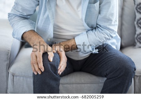 Old man suffering from knee pain sitting sofa Royalty-Free Stock Photo #682005259