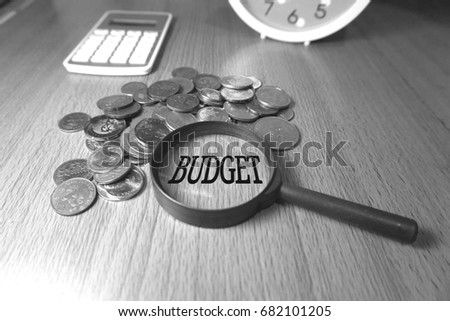 Conceptual photos of coins, magnifying glass, calculator and wooden background to show financial matters. Selective focused with textual term regarding budget in black and white