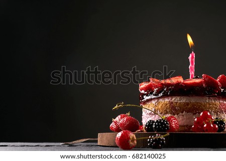 Wodden cake board with homemade raspberry-blackberry and strawberry birthday tart on dark stone table isolated on black background with copy space.