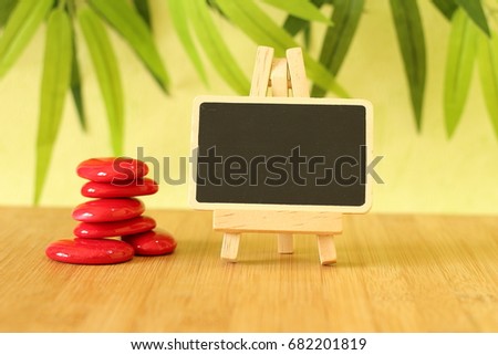 Small empty slate in width to write a message posed on the bamboo floor with red stones columns in the lifestyle Zen with a candle all on wooden floor and green foliage background