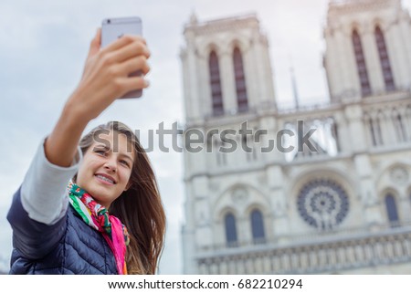 Teenager tourist girl is taking selfie on cathedral of Notre Dame de Paris with mobile smart phone. Travel, tourism, vacation concept. France.