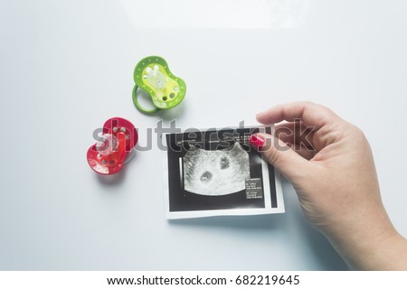 Twin pregnancy. Two soothers,an ultrasound picture of two babies and a mother's hand.