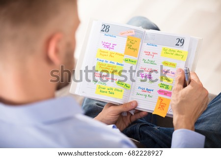 Close-up Of Man Writing Important Notes In Diary With Pen