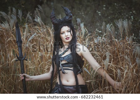 Beautiful wild girl with horns stands in the thickets