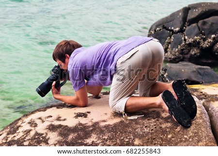 A young photographer takes a picture on a stony beach