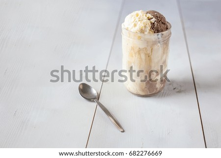 Delicious Vanilla and chocolate ice cream with granola cereal in a vintage glass jar against a wooden background 