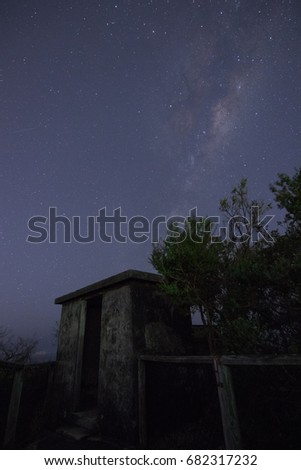 Milkyway in the night sky above abandoned concrete bunker and silhouette of trees
