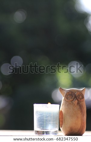  wooden owl doll and blue candle in small glass light point and white bokeh on green background