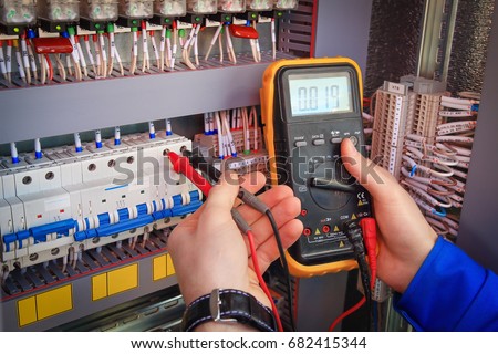 Multimeter is in hands of electrician on background of electrical automation cabinet. Adjustment of electrical control circuit for industrial equipment. Royalty-Free Stock Photo #682415344