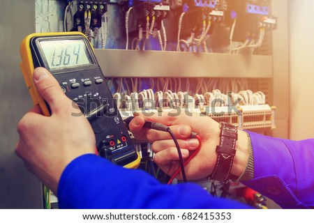 Multimeter in hands of electrician close-up against  background of electrical wires and relays. Adjustment of scheme of automation and control of electrical equipment Royalty-Free Stock Photo #682415353