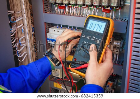 Electrical Engineer adjusts electrical equipment with a multimeter in his hand closeup. Professional electrician in electric automation cabinet Royalty-Free Stock Photo #682415359