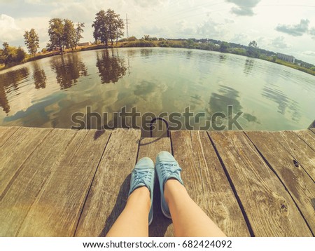 girl in blue shoes sits on the old wharf in the lake on a sunny day. Caucasian. Royalty-Free Stock Photo #682424092