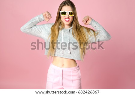 Portrait of young attractive funny teenager girl with shrtaight blonde hair and sunglasses in trendy clothes on the pink background, studio shooting. angry amused emotion