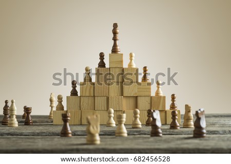 Business hierarchy; ranking and strategy concept with chess pieces standing on a pyramid of wooden building blocks with the king at the top with copy space. Royalty-Free Stock Photo #682456528