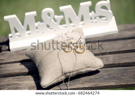 On a wooden floor a sign Mr & Mrs and a pillow with golden wedding rings