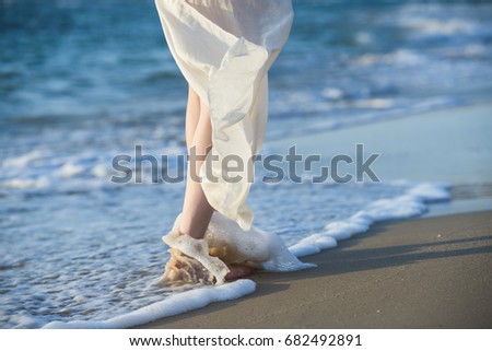 Beautiful woman in a white dress walking along the edge of the beach during a sunset. Horizon line