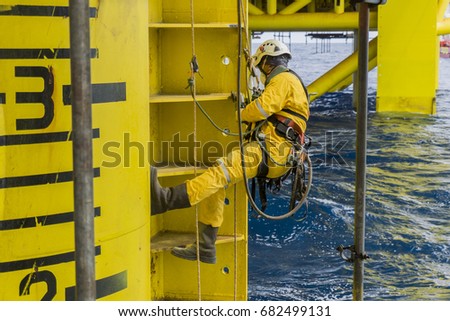 Working at height. A commercial abseiler with respiratory protection and fall arrestor device hanging on oil and gas platform jacket module to clean rust using air grinding machine. Royalty-Free Stock Photo #682499131