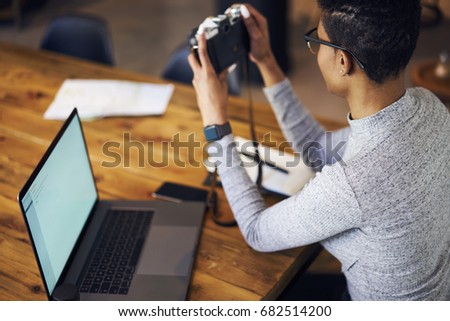 Back view of skilled afro american woman photographer taking picture of office interior for uploading files on laptop with mock up screen,rear view of female freelancer making amateur pictures for web