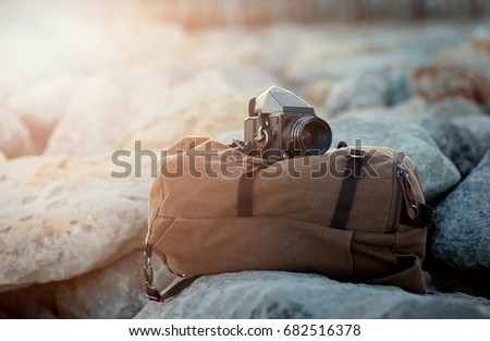 The old film medium format camera lies on the rocks against the backdrop of a canvas vintage backpack for travel