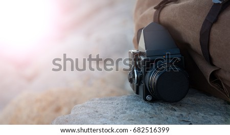 The old film medium format camera lies on the rocks against the backdrop of a canvas vintage backpack for travel
