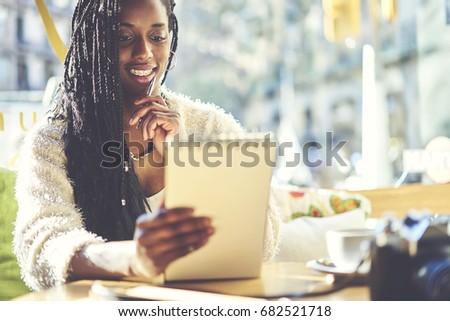 Smiling female journalist proofreading article for publication holding notepad with text sitting in cafe, creative designer thinking about improvement graphic solving problems in cozy coffee shop