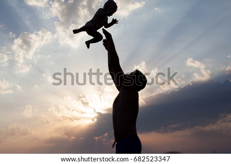 Dad plays with young son silhouette at sunset