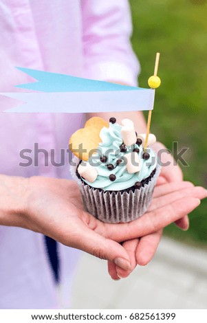Delicious cupcake with blue cream and marshmallows in the hands of the girls. Sweet gift for birthday and wedding. Ribbon with place for text