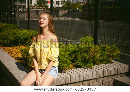 Young beautiful woman is strolling outdoors in the yard, against the backdrop of greenery and houses, warm summer sunny day