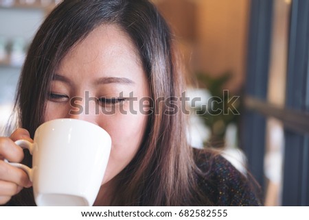 Closeup image of asian woman holding and drinking hot coffee with feeling good and smiley face