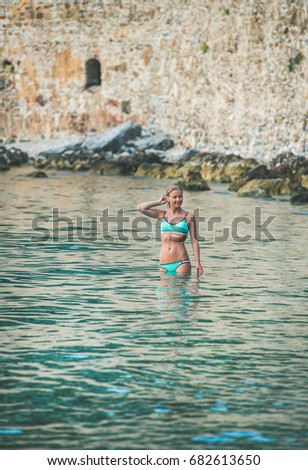 Young beautiful slavian woman tourist wearing turquoise bikini enjoying sea at beach near ancient fortress wall and shipyard in city center of Alanya, Mediterranean Turkey