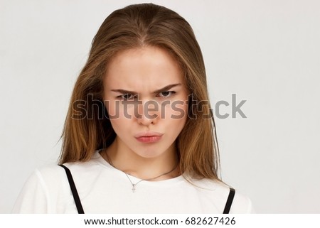 Young beautiful cute girl showing different emotions. Background for the girl a concrete gray wall.Portrait of outraged young woman, frowning her eyebrows being displeased with something. 