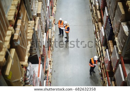 Above view of warehouse workers group in aisle between rows of tall shelves full of packed boxes and goods Royalty-Free Stock Photo #682632358