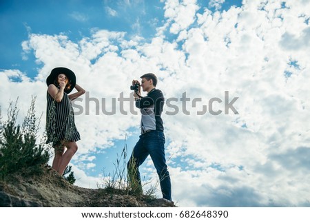 young couple on the hill, man taking picture of his girlfriend that posing in dress