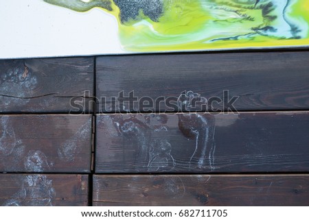 Young woman artist paints acrylic paint on nature on a wooden pier. Traces of her legs remained with paint on a wooden background.