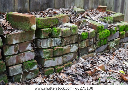 Piles of used red bricks against a wood fence