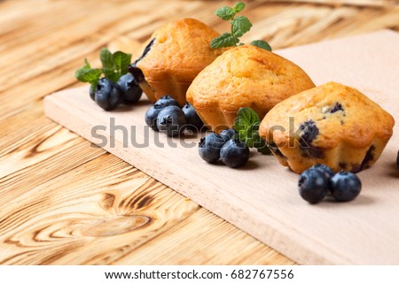 Blueberry muffin - homemade baked cupcakes with fresh berries on wooden background. Top view of delicious bakery dessert.