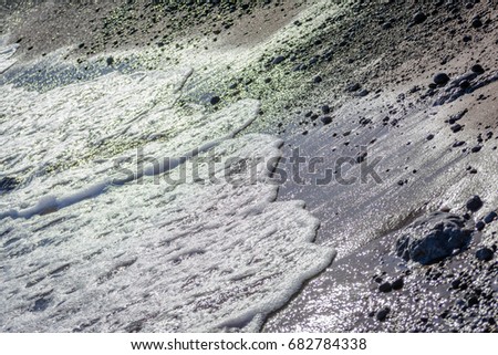 Sea waves with white foam on sand beach with stones. Contrast picture, catty-corner shot.