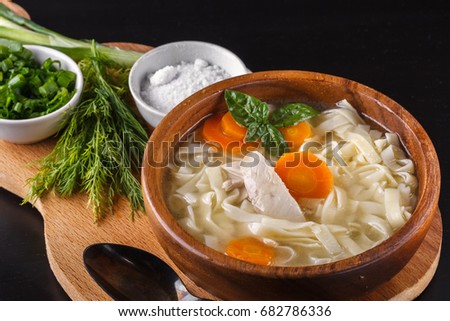 Homemade chicken noodle soup with carrots and fresh basil in a wooden bowl on a wooden board with salt, dill and green onions Royalty-Free Stock Photo #682786336