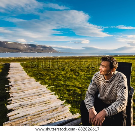 Portrait norway landscape nature of the mountains of Spitsbergen Longyearbyen Svalbard man  in sweater with beard smiling lyifestyle on a polar day  arctic summer in the sunset and blue cloudly sky  